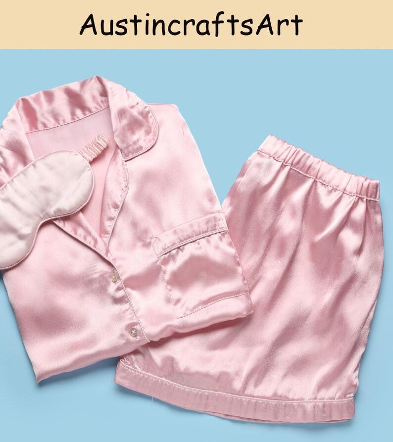 May include: A light pink pajama set featuring a button-down shirt with a collar and a chest pocket, paired with matching elastic-waist shorts and a coordinating sleep mask. The fabric has a smooth, satin-like finish. Text reads AustincraftsArt.