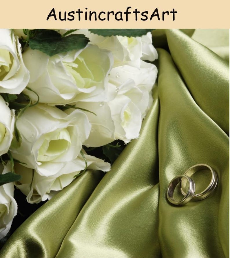 May include: A bouquet of white roses with green leaves resting on a draped olive green satin fabric next to two metallic rings. The text AustincraftsArt is visible at the top of the image. The composition features soft lighting and floral textures.
