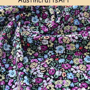 K&ouml;nnte beinhalten: Stoff mit schwarzem Hintergrund und einem dichten Blumenmuster in den Farben Violett, Hellblau, Gelb und Wei&szlig;. Das Textil zeigt eine wiederkehrende Anordnung kleiner Bl&uuml;ten und gr&uuml;ner Bl&auml;tter sowie den Text AustincraftsArt und #9.