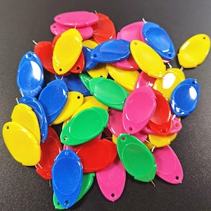 May include: A pile of colorful oval-shaped plastic charms in red, yellow, blue, green, and pink. The charms have a small hole at the top for attaching to a necklace or bracelet.