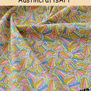 K&ouml;nnte beinhalten: Stoff mit einem sich wiederholenden Muster aus wei&szlig;en Hufeisen mit schwarzer Umrandung vor einem Hintergrund aus strahlenf&ouml;rmigen gelben, rosa und blauen Sonnenstrahlen. Der Text AustincraftsArt steht oben und #13 unten rechts.