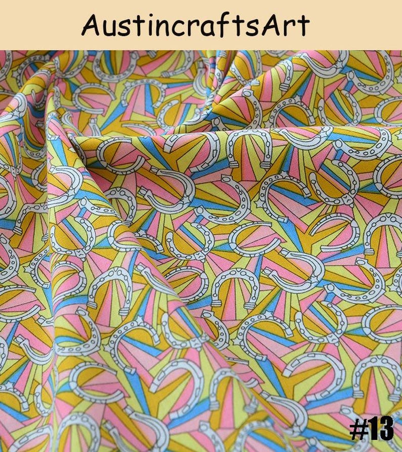 K&ouml;nnte beinhalten: Stoff mit einem sich wiederholenden Muster aus wei&szlig;en Hufeisen mit schwarzer Umrandung vor einem Hintergrund aus strahlenf&ouml;rmigen gelben, rosa und blauen Sonnenstrahlen. Der Text AustincraftsArt steht oben und #13 unten rechts.