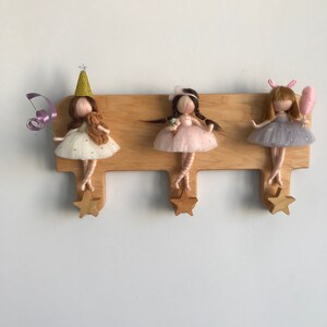 May include: Three wooden doll hooks with star-shaped ends. Each hook features a felt doll with a different outfit and accessories. The dolls are wearing dresses and have long hair. One doll is wearing a party hat, another is holding an ice cream cone, and the third is holding a pink cotton candy.