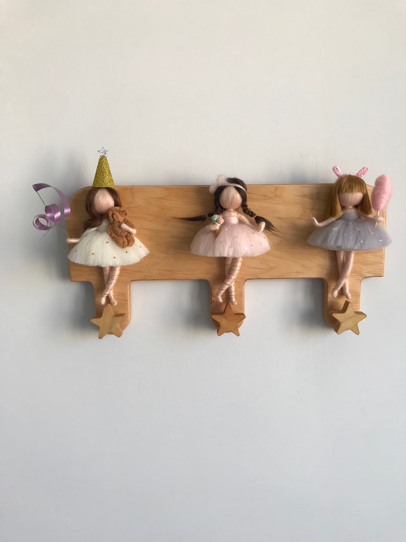 May include: Three wooden doll hooks with star-shaped ends. Each hook features a felt doll with a different outfit and accessories. The dolls are wearing dresses and have long hair. One doll is wearing a party hat, another is holding an ice cream cone, and the third is holding a pink cotton candy.