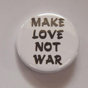 May include: A white button badge with the message "MAKE LOVE NOT WAR" in black lettering. The text is arranged in four lines. The badge is circular and has a shiny surface.