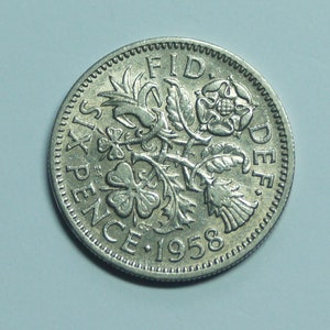 May include: A 1958 Six Pence coin. The silver coin displays floral emblems, including a rose and shamrocks, with the text "SIX PENCE" and the year "1958". The coin has a detailed, textured edge.
