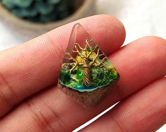 May include: A triangular resin pendant with a wire-wrapped tree of life design. The tree is made of copper wire and has green and yellow resin leaves. The pendant is set in a brown resin base.