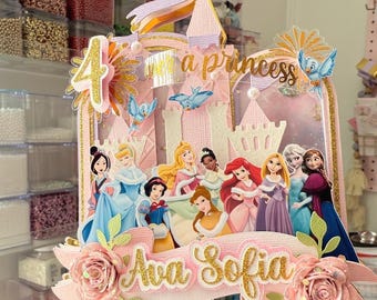 May include: A pink and gold princess-themed cake topper featuring a castle, the number 4, and the text "Ava Sofia." The topper includes images of various Disney princesses and decorative flowers.