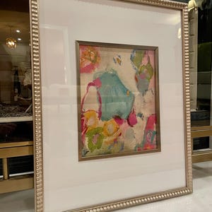 May include: A framed abstract painting with a white mat and a gold frame. The painting features a variety of colors including pink, blue, green, and yellow. The painting is abstract and features a variety of shapes and textures.