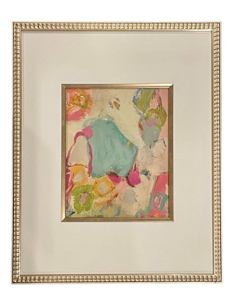 May include: A framed abstract painting with a white background and colorful paint strokes in shades of pink, blue, green, and yellow.