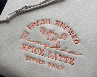May include: A light gray hoodie with an orange embroidered design that says "Fresh Brewed Pumpkin Spice Latte Served Daily".