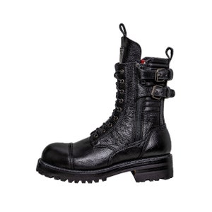May include: Black leather combat boot with a textured finish. The boot features a cap toe, lace-up closure, side zipper, and two buckle straps. The sole is thick and lugged.