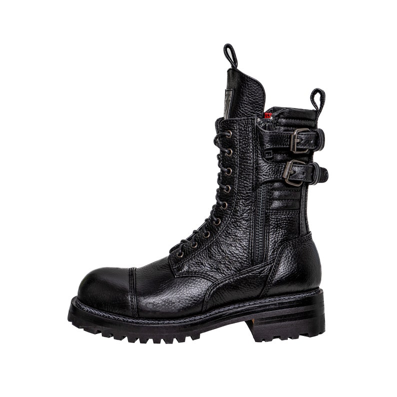 May include: Black leather combat boot with a textured finish. The boot features a cap toe, lace-up closure, side zipper, and two buckle straps. The sole is thick and lugged.