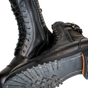 May include: Black leather boots with a textured finish. The boots have a lace-up design, side zippers, and a rugged sole. The tall boots are designed for durability and style. The soles have a heavy tread for traction.