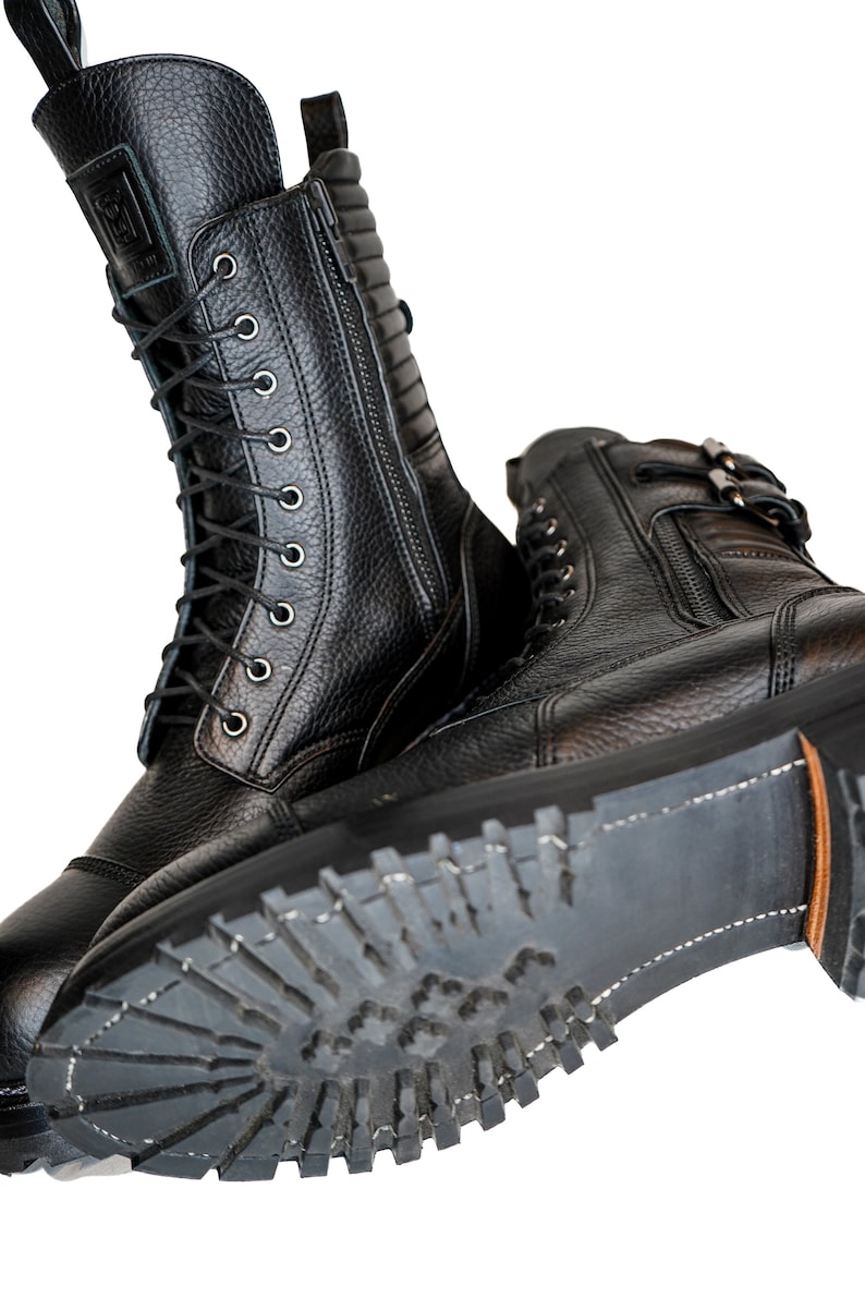 May include: Black leather boots with a textured finish. The boots have a lace-up design, side zippers, and a rugged sole. The tall boots are designed for durability and style. The soles have a heavy tread for traction.