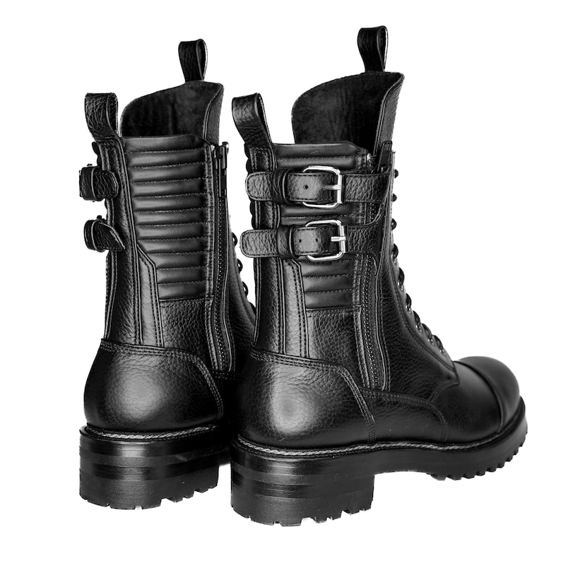 May include: Black leather combat boots with multiple buckles and a side zipper. The boots have a textured finish, a rounded toe, and a lug sole. The boots have a pull tab at the top of the shaft.