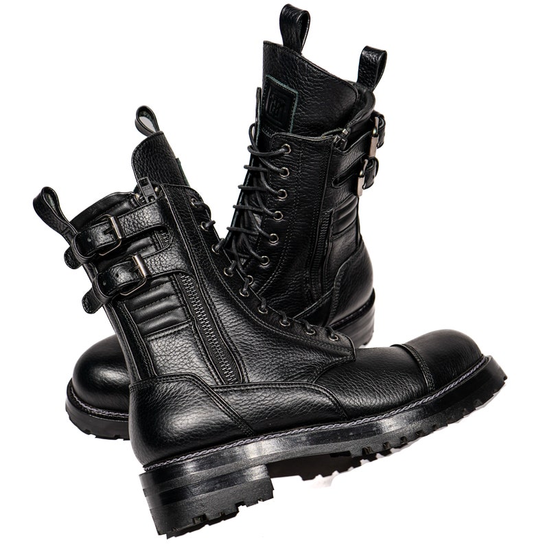 May include: Pair of black leather combat boots with multiple buckles, zippers, and laces. The boots have a thick, lugged sole and a rounded toe. The leather has a textured appearance. The boots are designed for durability and style.