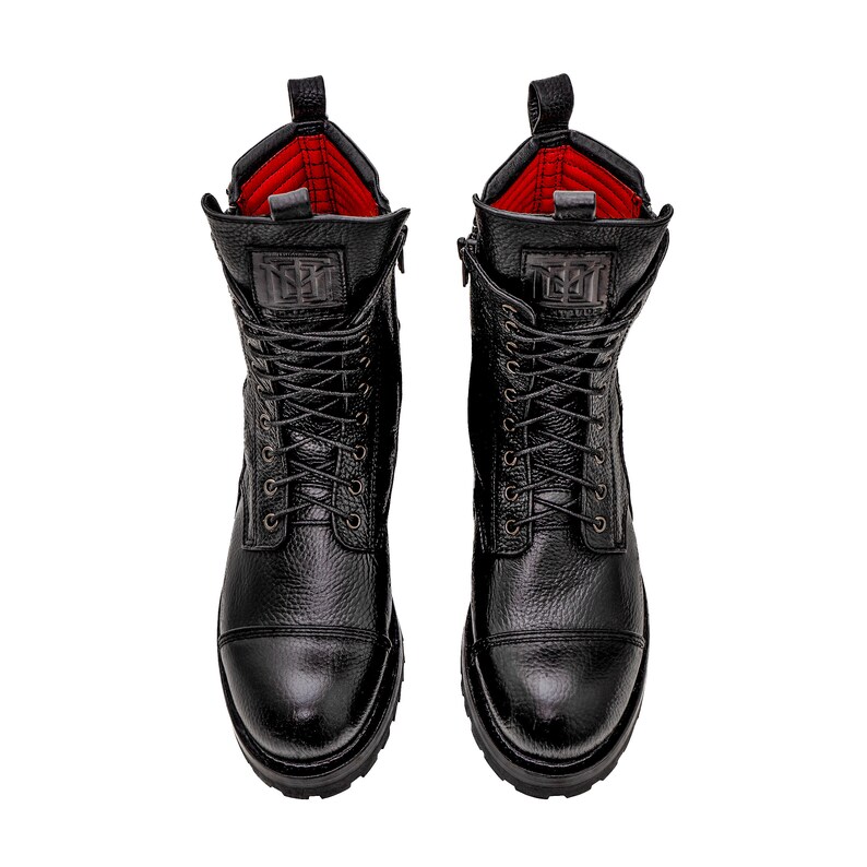 May include: Pair of black leather combat boots with a textured finish. The boots feature a lace-up design, side zippers, and a red interior lining. The boots have a lug sole and a logo on the tongue.