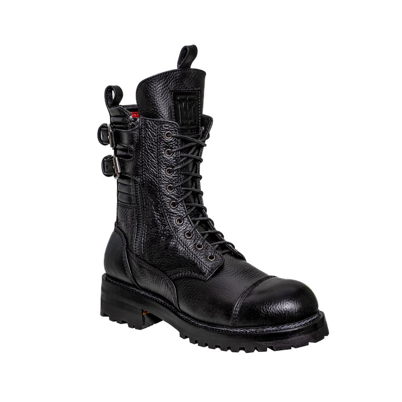 May include: Black leather combat boot with a textured finish. The boot features a lace-up design, two buckle straps, and a pull tab at the top. The sole is thick and lugged.