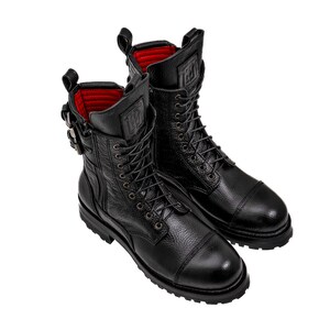 May include: A pair of black leather combat boots with a textured finish. The boots feature a lace-up design, a side zipper, and a buckle closure. The interior lining is red. The boots have a cap toe and a thick sole.