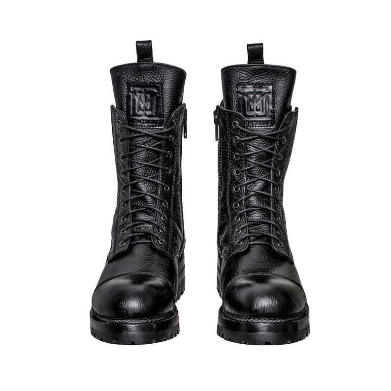 May include: A pair of black leather combat boots with a textured finish. The boots have a lace-up design, side zippers, and a logo embossed on the tongue. The soles are thick and lugged.