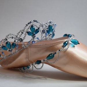 May include: A pair of ballet shoes decorated with a beaded crown featuring teal and silver beads.