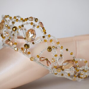 May include: A delicate gold and clear crystal beaded crown, designed for a ballerina's pointe shoe.
