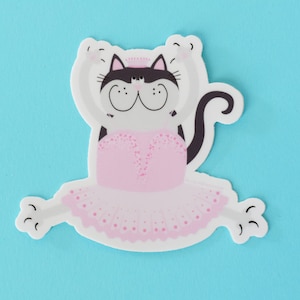 May include: A white cat wearing a pink tutu and a crown, with black ears and tail, is in a ballet pose on a light blue background.