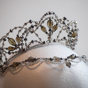 May include: A silver and brown beaded tiara with a delicate design. The tiara is made with small, clear beads and larger, brown beads.
