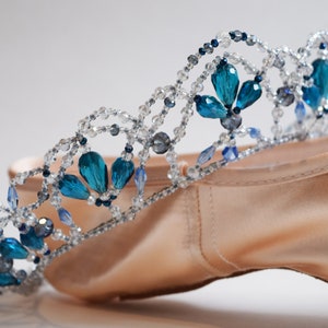 May include: A delicate crown made of silver beads and blue crystals, resting on a pair of ballet shoes.