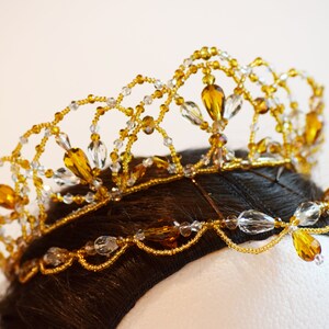 May include: A gold crown with clear and amber beads. The crown is made of wire and beads, and it is decorated with a pattern of leaves and flowers.