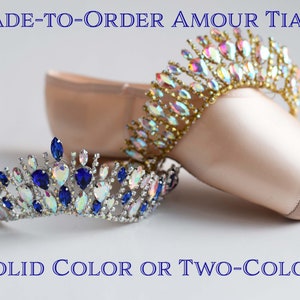 May include: Two jeweled tiaras, one with blue and clear stones and one with iridescent stones, are displayed on a ballet shoe. The text "MADE-TO-ORDER AMOUR TIARA" and "SOLID COLOR OR TWO-COLOR" is visible below the tiaras.