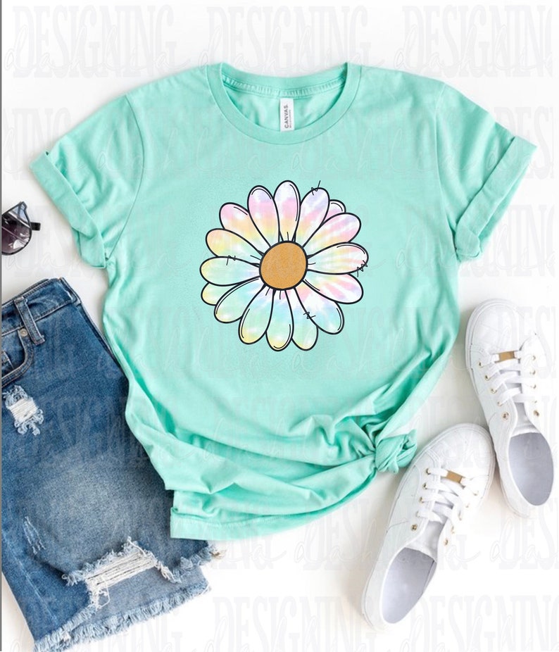 K&ouml;nnte beinhalten: Ein hellgr&uuml;nes T-Shirt mit einem Batik-G&auml;nsebl&uuml;mchen-Design. Die Blume hat eine gelbe Mitte und regenbogenfarbene Bl&uuml;tenbl&auml;tter.