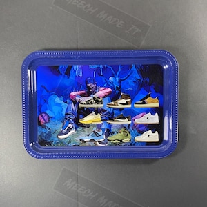 Puede incluir: Una bandeja de metal azul con un gráfico de una persona que lleva una chaqueta de camuflaje y varios pares de zapatillas. El fondo es una escena de bosque azul y morado.