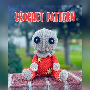 May include: Crochet pattern for a grey and orange plush toy with a stitched-on face. The toy is sitting on a brick wall. The text "CROCHET PATTERN" is at the top of the image.