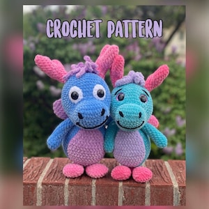 Könnte beinhalten: Zwei gehäkelte Plüschdrachenspielzeuge, eines blau und eines türkis, mit rosa Akzenten. Die Drachen lächeln und haben große, schwarze Augen. Der Text "CROCHET PATTERN" befindet sich oben im Bild.