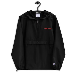 May include: Black Champion windbreaker jacket with a red embroidered "TRD PRO" logo on the front. The jacket has a zipper closure and a hood.