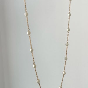 May include: A delicate gold-toned chain necklace featuring evenly spaced, small, round, white pearls. The necklace consists of a thin metal link chain with individual pearls integrated at regular intervals along the entire length of the jewellery piece.