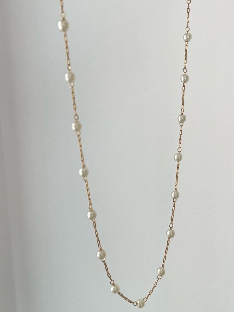 May include: A delicate gold-toned chain necklace featuring evenly spaced, small, round, white pearls. The necklace consists of a thin metal link chain with individual pearls integrated at regular intervals along the entire length of the jewellery piece.