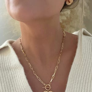 K&ouml;nnte beinhalten: Goldfarbenes Schmuckset mit einer Herzanh&auml;nger-Halskette und passenden Ohrsteckern. Die Halskette hat ein Kettenglied-Design mit Knebelverschluss und einem strukturierten Herzanh&auml;nger. Die Ohrringe sind rund mit einem strukturierten, geschichteten Design.