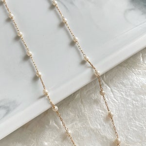 May include: A delicate gold chain necklace featuring evenly spaced, small white pearls integrated along the length of the metal links. The necklace is composed of a thin, polished gold-tone chain with round, lustrous white pearls attached at regular intervals.