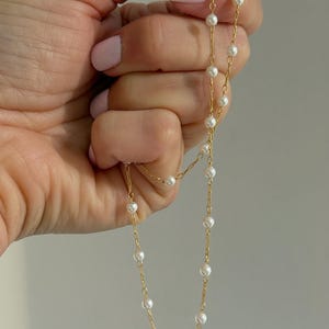 May include: A delicate gold chain necklace featuring evenly spaced small white pearls along the length of the links. The necklace is constructed with a thin metallic gold chain and round, smooth white pearls that are integrated into the chain design.