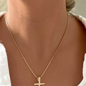 Puede incluir: Un collar de cadena de oro con un peque&ntilde;o colgante de cruz detallado.