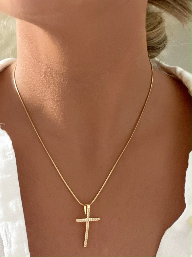 Puede incluir: Un collar de cadena de oro con un peque&ntilde;o colgante de cruz detallado.