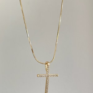 Puede incluir: Un collar de cadena dorada con un peque&ntilde;o colgante de cruz brillante.