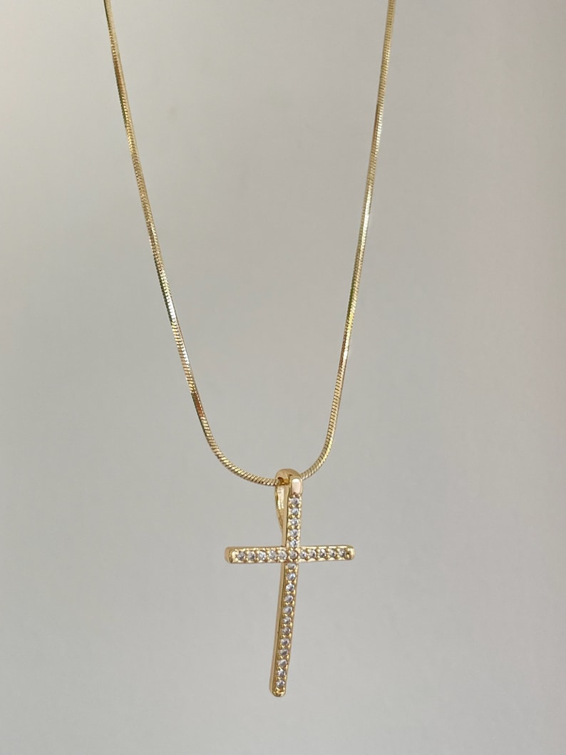 Puede incluir: Un collar de cadena dorada con un peque&ntilde;o colgante de cruz brillante.