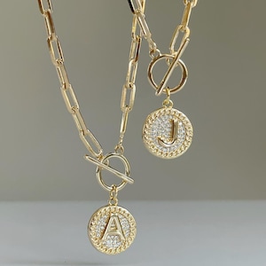 May include: Two gold necklaces with toggle clasps and round pendants featuring the letters "A" and "J" encrusted with clear rhinestones.