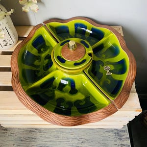 May include: A green and blue ceramic serving dish with a wooden rim. The dish is divided into four sections and has a small, round, lidded bowl in the center. The bowl has a wooden lid with a gold knob. The dish has a "Stoneware" label on the side.