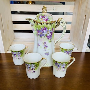 May include: A white ceramic mug with a black handle and the text "But First, Coffee" in a black, bold font. The mug is on a white surface.