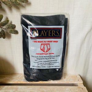 May include: A package of black underwear with the text "PLAYERS" and "1 BIG MAN'S FLY FRONT BRIEF". The packaging also includes details about the product's features, such as being shrink-resistant and designed for big or tall men.